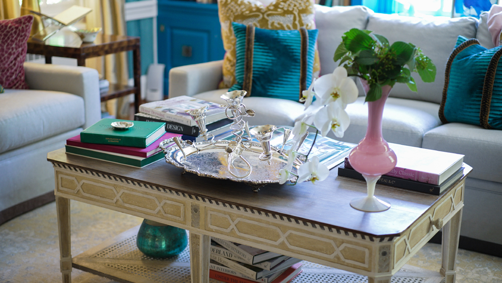 Living room vignette features a silver epergne centerpiece along with a collection of assorted coffee table books and decoration on a coffee table.